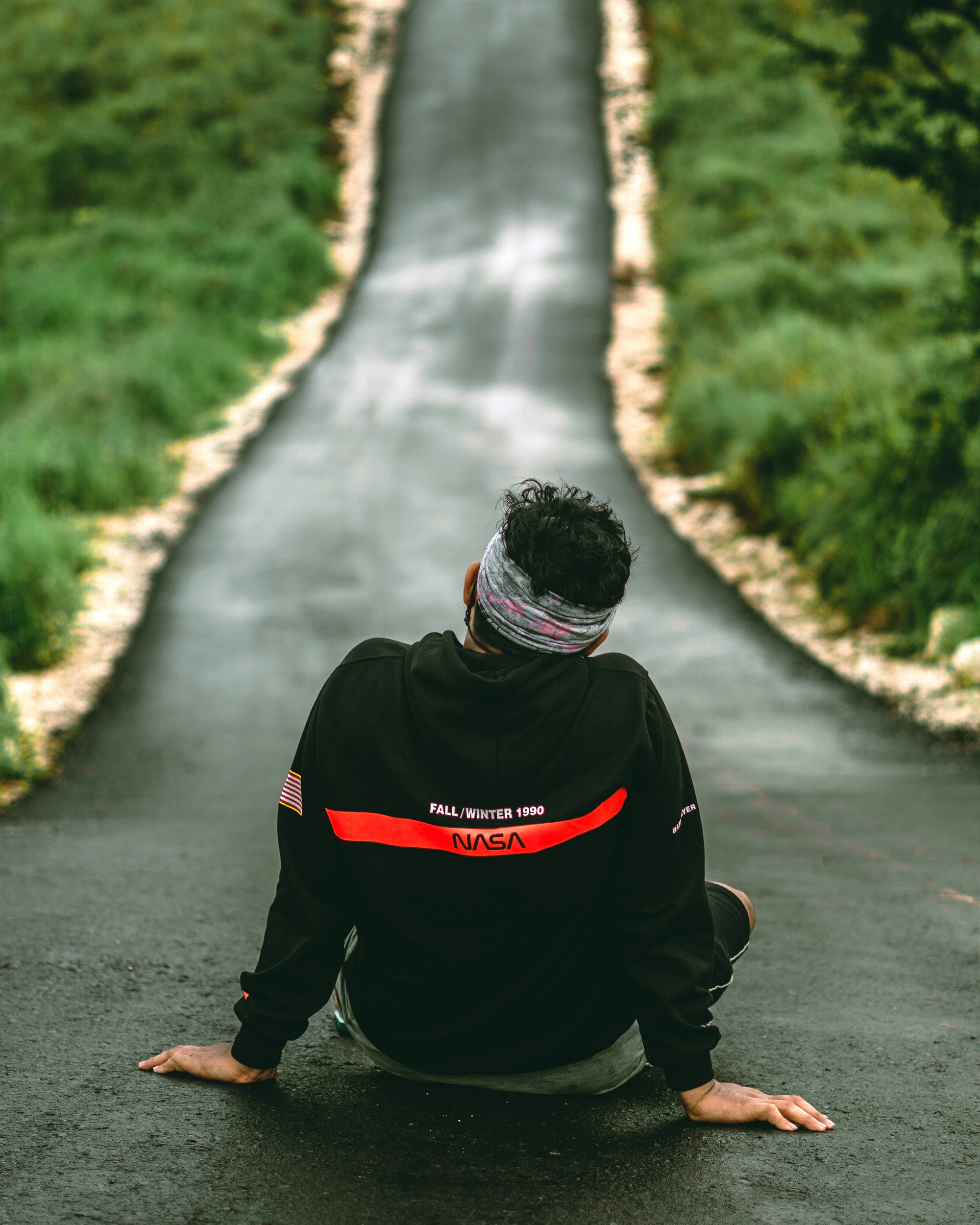 man in black and red hoodie walking on gray concrete road during daytime